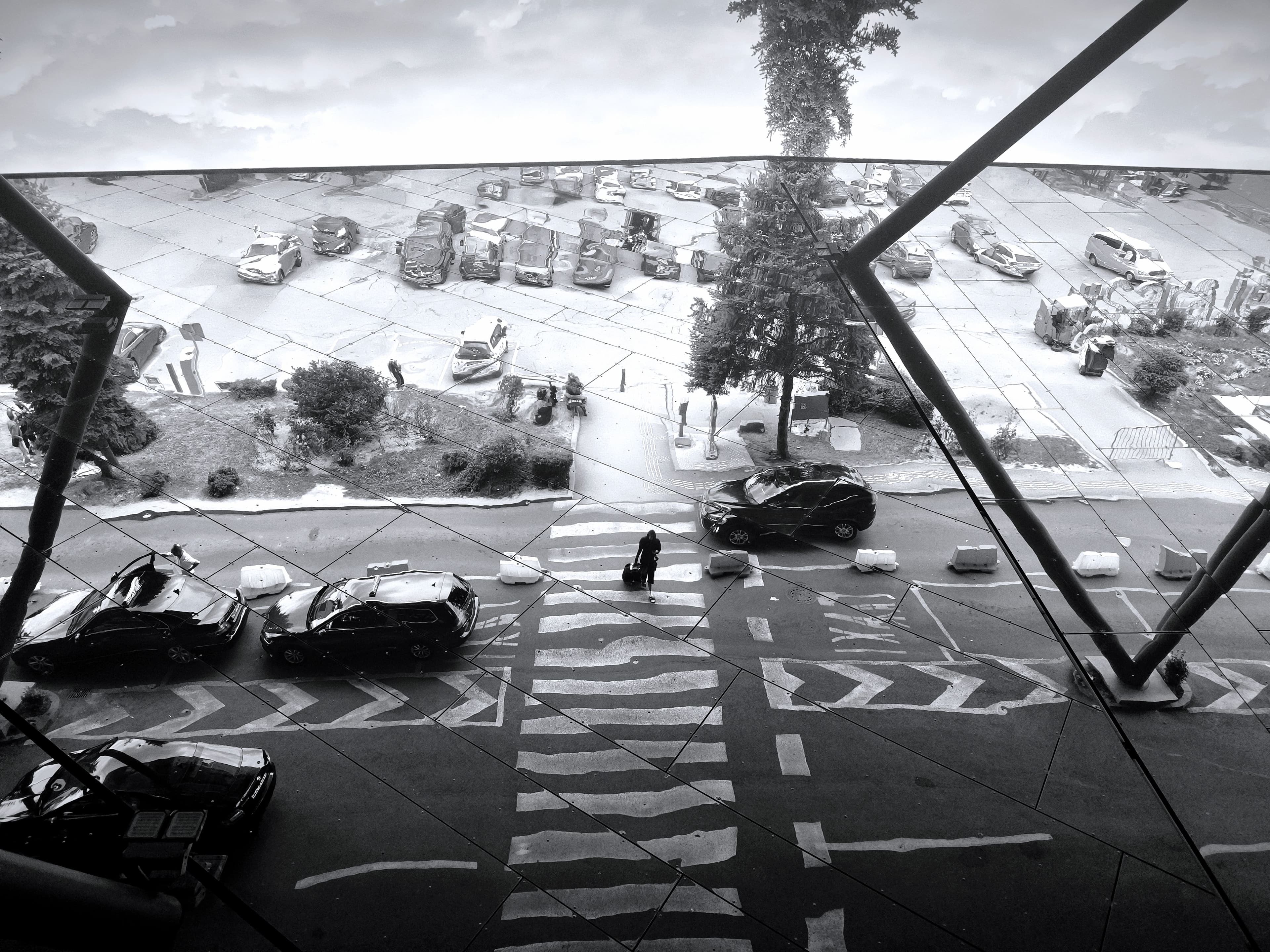 Taxis and a traveller with a suitcase reflected in the glass facade of a terminal