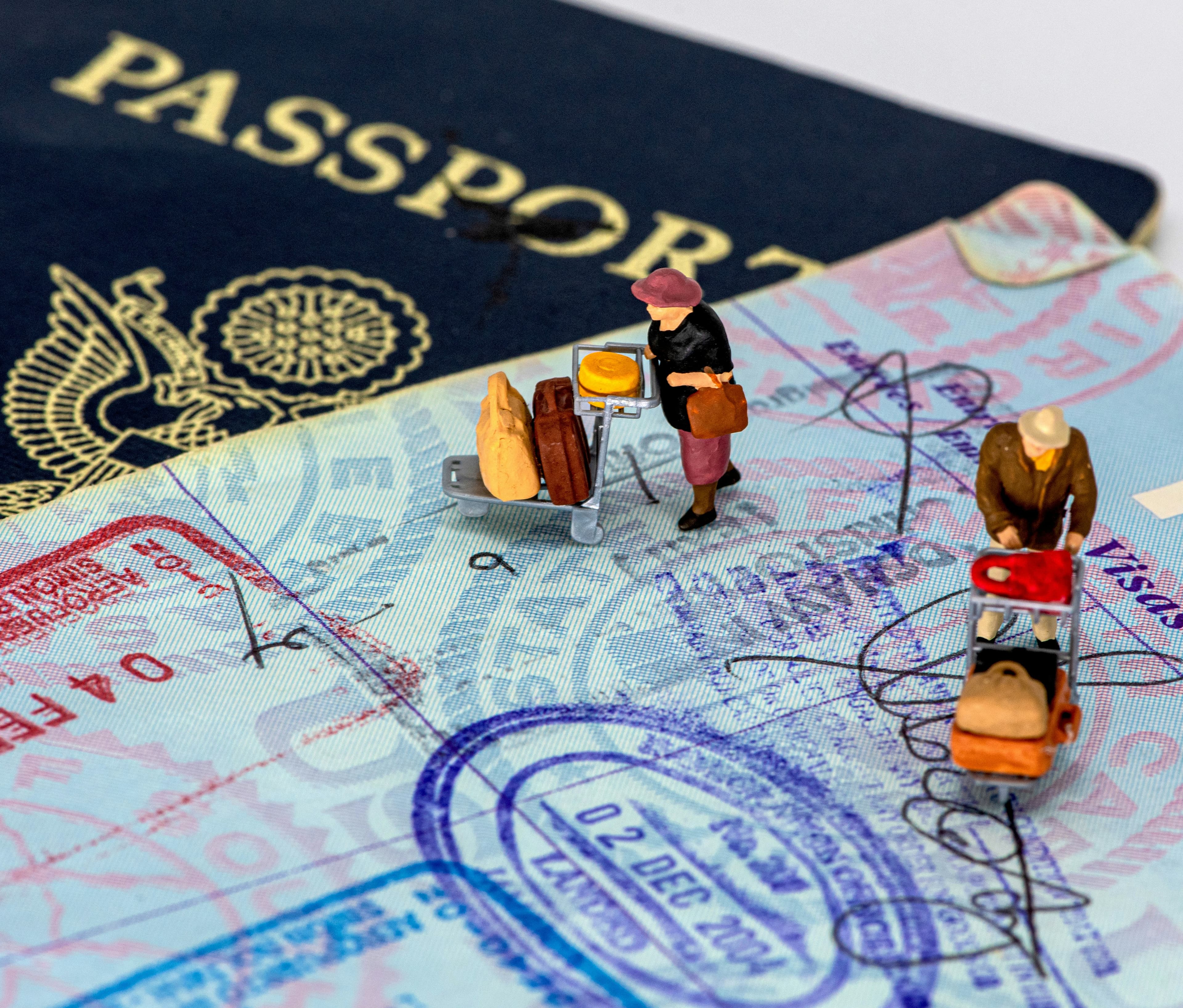 A passport with entry stamps and two miniature travellers with luggage